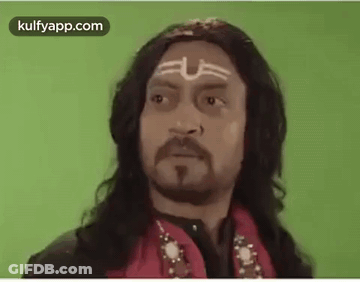 A Man With Long Hair , A Beard And A Tattoo On His Forehead Is Wearing A Red Jacket . GIF
