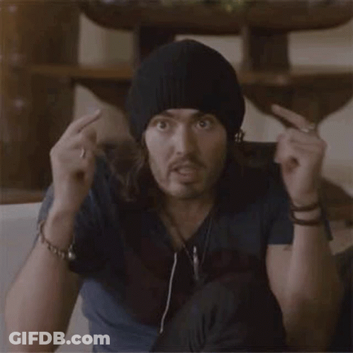 A Man With Long Hair And A Beanie Is Sitting On A Couch Making A Surprised Face . GIF