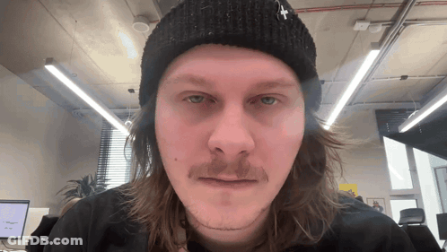 A Man With Long Hair And A Beanie With A Cross On It GIF