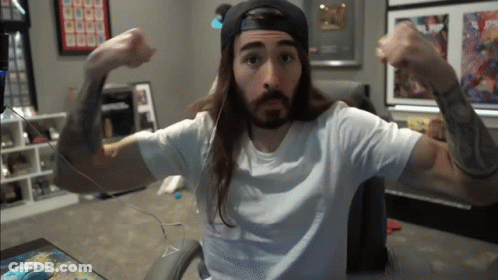 A Man With Long Hair And A Beard Is Flexing His Arms GIF