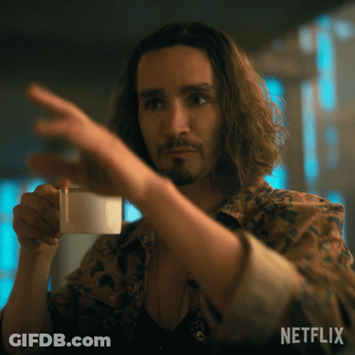 A Man With Long Hair And A Beard Is Holding A Cup Of Coffee And Pointing At It With A Netflix Logo In The Background GIF