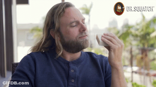 A Man With Long Hair And A Beard Is Holding A Napkin In Front Of A Dr. Squatch Logo GIF