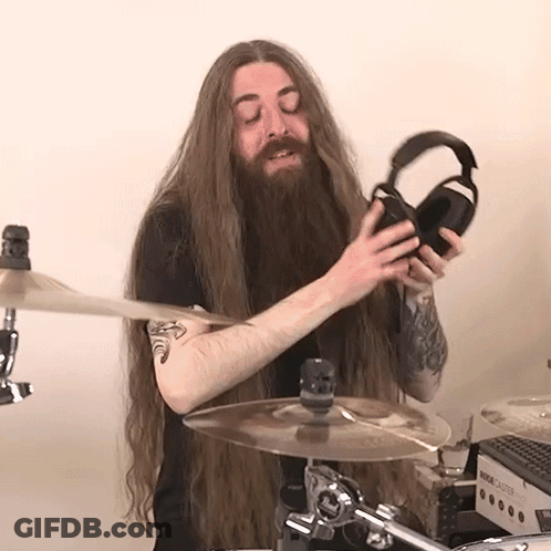 A Man With Long Hair And A Beard Is Holding A Pair Of Headphones While Playing Drums GIF