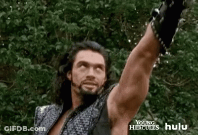 A Man With Long Hair And A Beard Is Holding A Sword In The Air . GIF