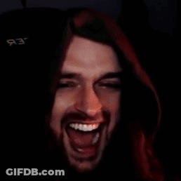 A Man With Long Hair And A Beard Is Laughing In A Dark Room With A Black Background GIF