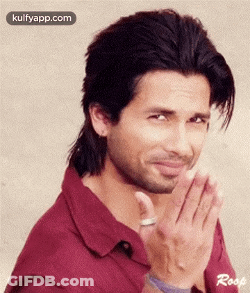 A Man With Long Hair And A Beard Is Making A Funny Face With His Hands Folded . GIF