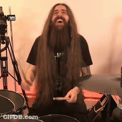 A Man With Long Hair And A Beard Is Playing A Drum Set GIF