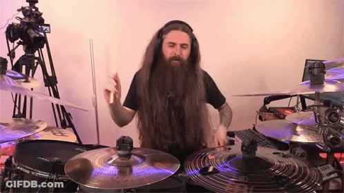 A Man With Long Hair And A Beard Is Playing Drums In Front Of A Camera GIF