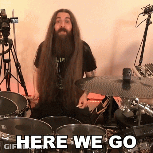 A Man With Long Hair And A Beard Is Playing Drums With The Words Here We Go Behind Him GIF