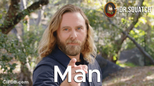 A Man With Long Hair And A Beard Is Pointing At The Camera And The Word Man Is On The Front Of His Shirt GIF