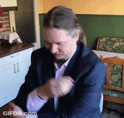 A Man With Long Hair And A Beard Is Sitting At A Table GIF