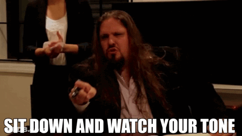 A Man With Long Hair And A Beard Is Sitting Down And Says Sit Down And Watch Your Tone GIF