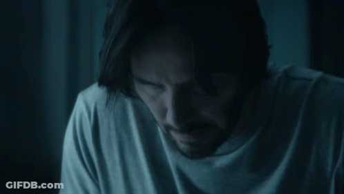 A Man With Long Hair And A Beard Is Sitting In A Dark Room . GIF