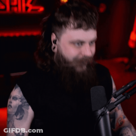 A Man With Long Hair And A Beard Is Sitting In Front Of A Microphone GIF
