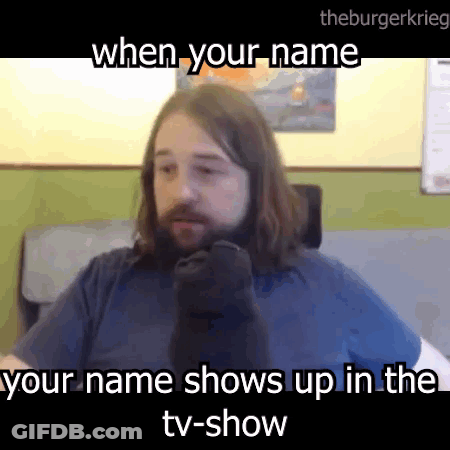 A Man With Long Hair And A Beard Is Sitting In Front Of A Tv And Talking On A Cell Phone . GIF