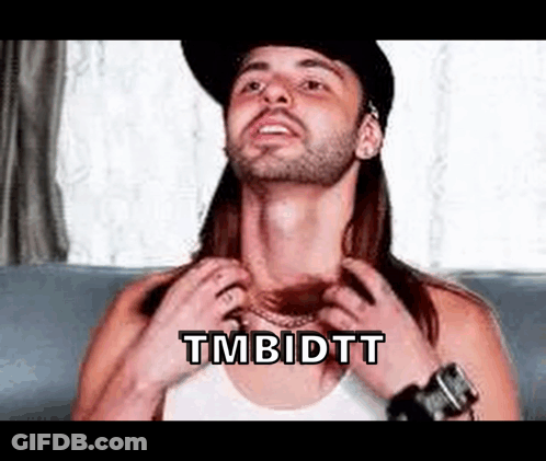 A Man With Long Hair And A Beard Is Sitting On A Couch Adjusting His Shirt . GIF