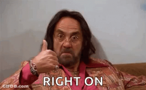 A Man With Long Hair And A Beard Is Sitting On A Couch And Giving A Thumbs Up . GIF