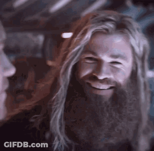 A Man With Long Hair And A Beard Is Smiling While Looking At Another Man . GIF