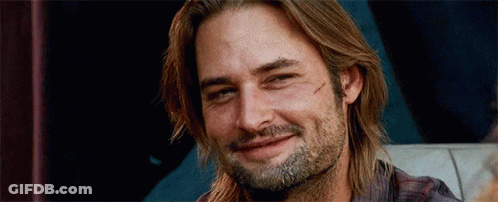 A Man With Long Hair And A Beard Is Smiling While Sitting On A Couch . GIF