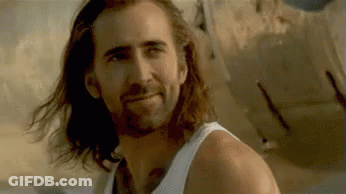 A Man With Long Hair And A Beard Is Smiling While Wearing A White Tank Top . GIF