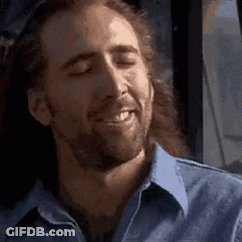 A Man With Long Hair And A Beard Is Smiling With His Eyes Closed In A Blue Shirt . GIF
