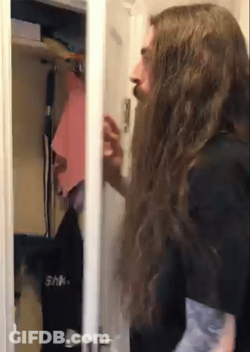 A Man With Long Hair And A Beard Is Standing In A Closet GIF