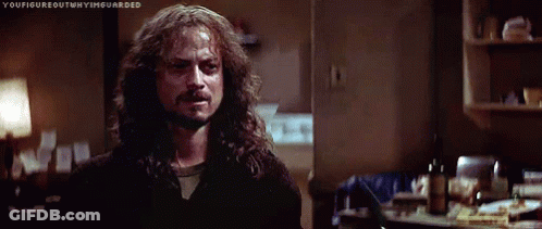 A Man With Long Hair And A Beard Is Standing In A Dark Room In A Kitchen . GIF