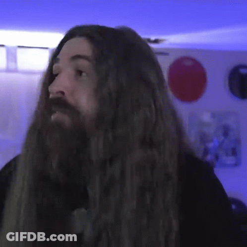 A Man With Long Hair And A Beard Is Standing In A Room GIF