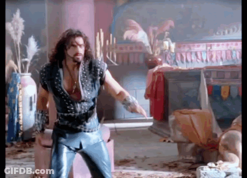 A Man With Long Hair And A Beard Is Standing In A Room With Candles On A Table . GIF