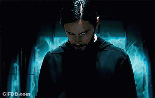A Man With Long Hair And A Beard Is Standing In Front Of A Blue Wall . GIF