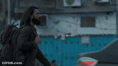 A Man With Long Hair And A Beard Is Standing In Front Of A Building GIF