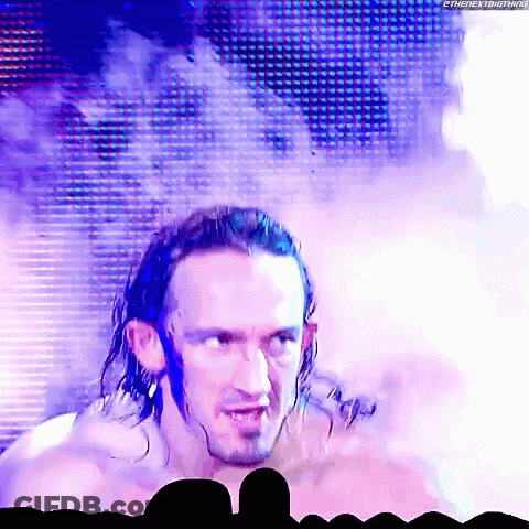 A Man With Long Hair And A Beard Is Standing In Front Of A Crowd And Smoke Is Coming Out Of His Head . GIF