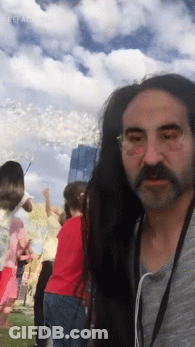 A Man With Long Hair And A Beard Is Standing In Front Of A Crowd Of People GIF