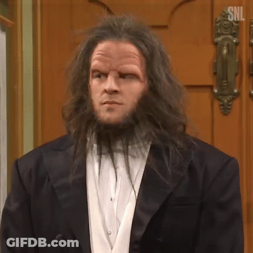 A Man With Long Hair And A Beard Is Standing In Front Of A Door . GIF