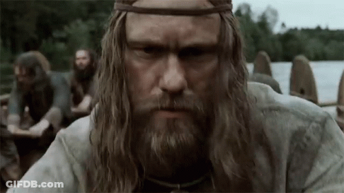 A Man With Long Hair And A Beard Is Standing In Front Of A Group Of Men In A Boat . GIF