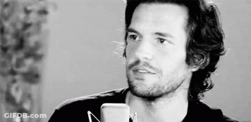 A Man With Long Hair And A Beard Is Standing In Front Of A Microphone In A Black And White Photo . GIF
