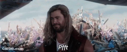 A Man With Long Hair And A Beard Is Standing In Front Of A Pile Of Flowers And Says Pfft GIF
