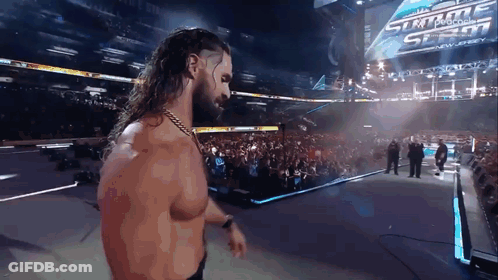 A Man With Long Hair And A Beard Is Standing In Front Of A Sign That Says Summerslam GIF