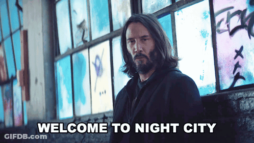 A Man With Long Hair And A Beard Is Standing In Front Of A Wall That Says Welcome To Night City On It GIF