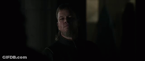 A Man With Long Hair And A Beard Is Standing In The Dark Looking At Something . GIF