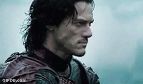 A Man With Long Hair And A Beard Is Standing In The Rain Looking At The Camera . GIF