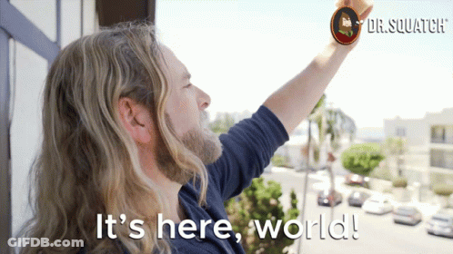 A Man With Long Hair And A Beard Is Standing On A Balcony With The Words " It 'S Here World " Above Him GIF