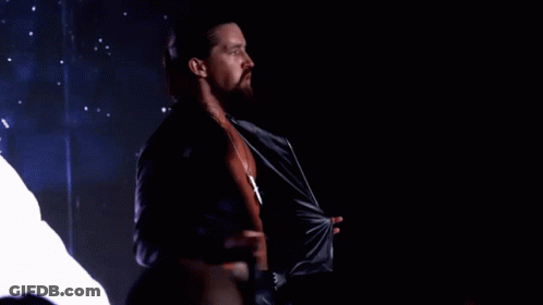 A Man With Long Hair And A Beard Is Taking Off His Shirt GIF