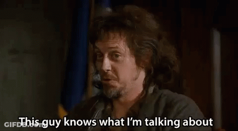 A Man With Long Hair And A Beard Is Talking On A Cell Phone While Holding A Gun . GIF