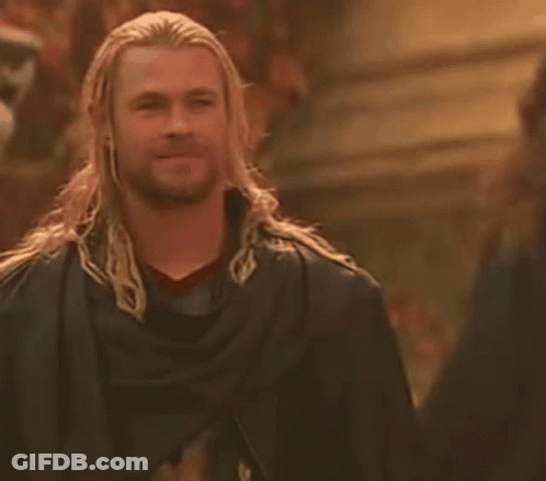 A Man With Long Hair And A Beard Is Wearing A Black Cape And Smiling . GIF