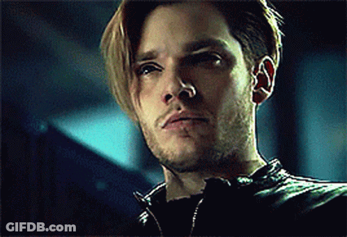 A Man With Long Hair And A Beard Is Wearing A Black Leather Jacket And Looking At The Camera . GIF