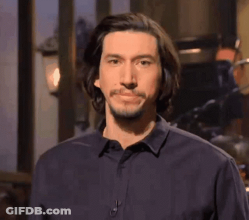 A Man With Long Hair And A Beard Is Wearing A Black Shirt And Looking At The Camera . GIF