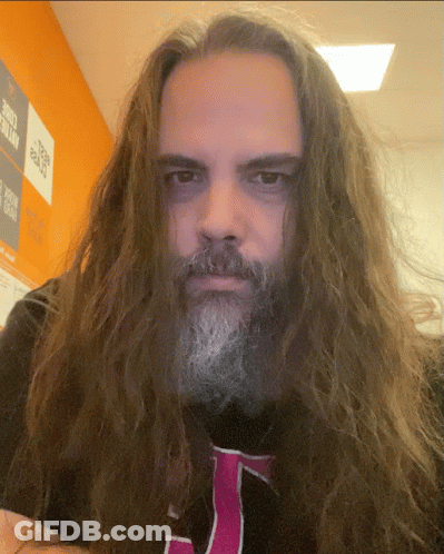 A Man With Long Hair And A Beard Is Wearing A Black Shirt With A Pink J On It GIF