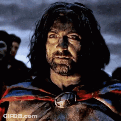 A Man With Long Hair And A Beard Is Wearing A Cape With A Medallion Around His Neck GIF