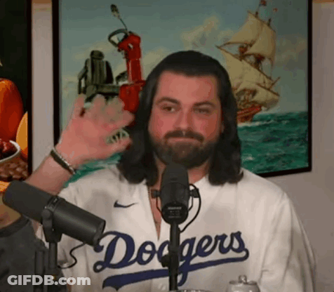 A Man With Long Hair And A Beard Is Wearing A Dodgers Jersey And Waving At The Camera . GIF